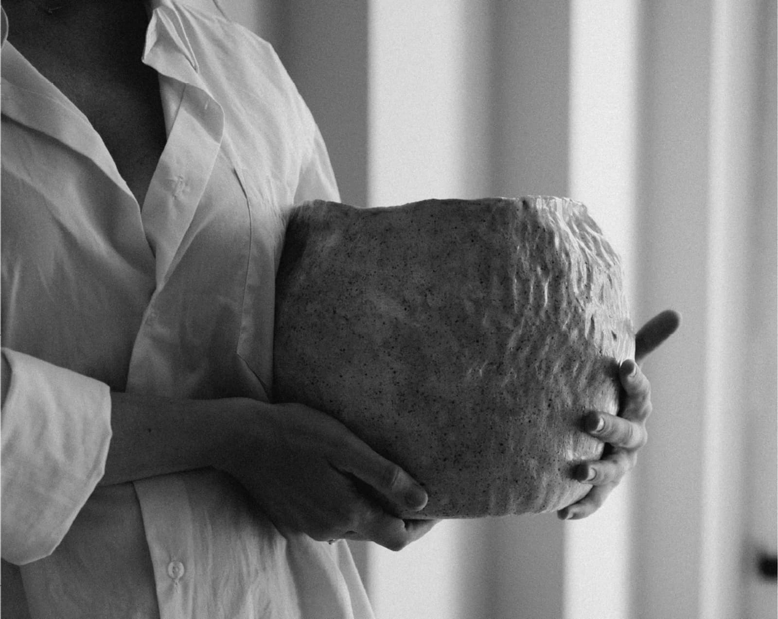 Une femme tenant délicatement un objet texturé contre sa poitrine, en noir et blanc